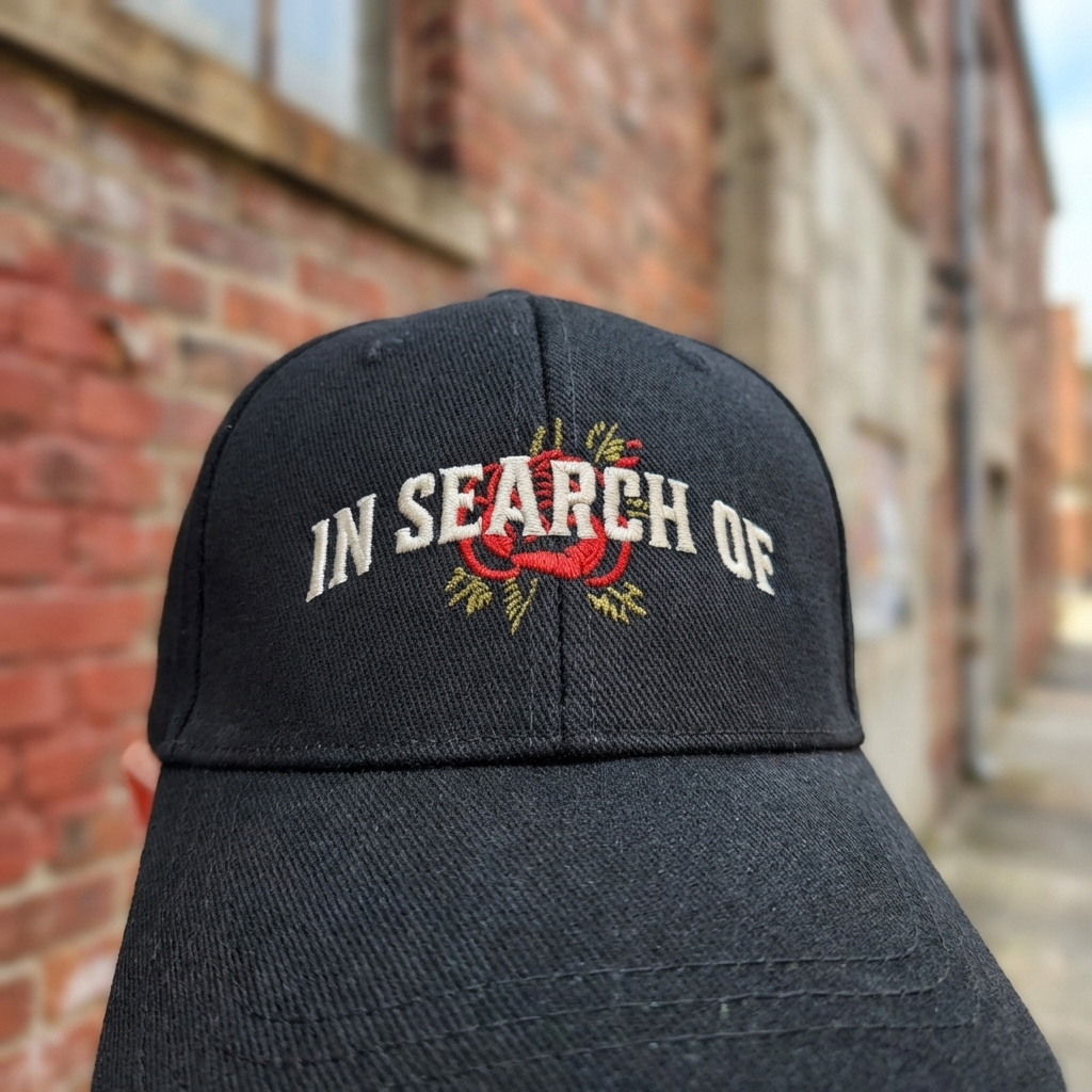 In Search Of Purpose Driven Cap close-up borduurwerk - wit serif logo en rood roos tattoo motief op zwarte cap
